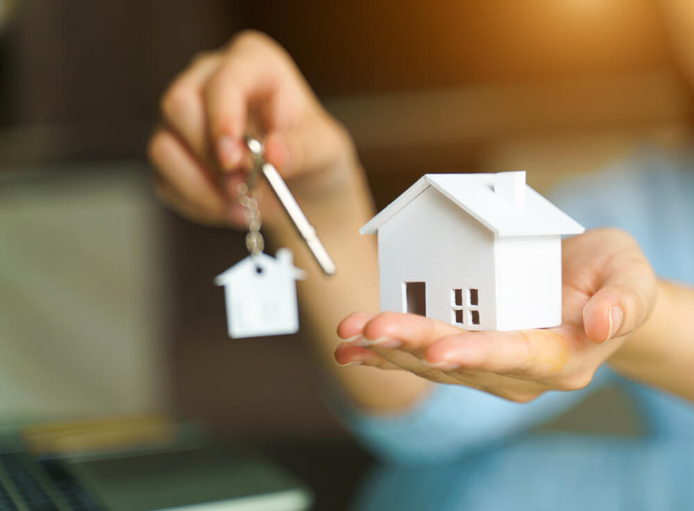 Agent za nekretnine drži model kuće i ključeve sa priveskom u ruci
