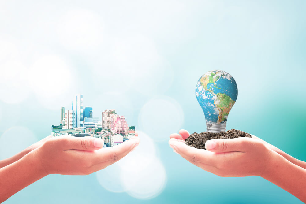 Ecology and Entrepreneurship Concept: Two Human Hand Hold Beautiful Big City and Blue Planet of Light Bulb