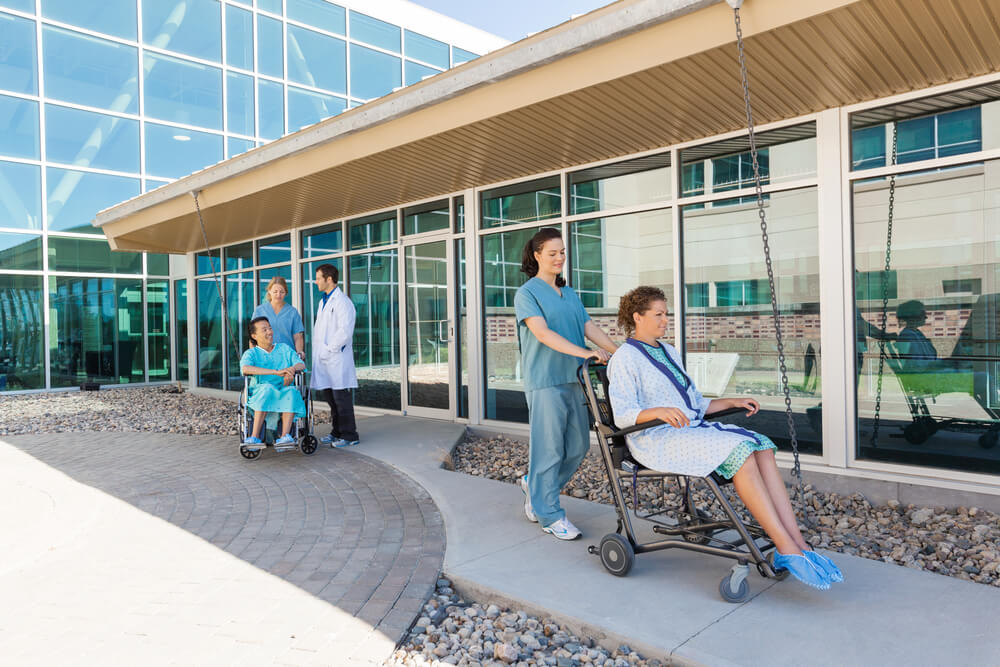Nurses and Male Doctor With Patients on Wheelchairs at Hospital Courtyard