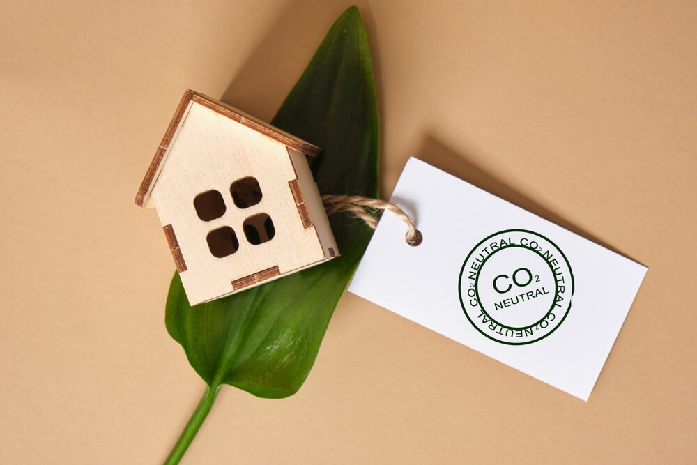 Green Leaves, Miniature Wooden House Model and White Tag With CO2 Neutral Marking on Brown Background, Eco House Concept, Environmentally Friendly Building, Zero Waste Lifestyle