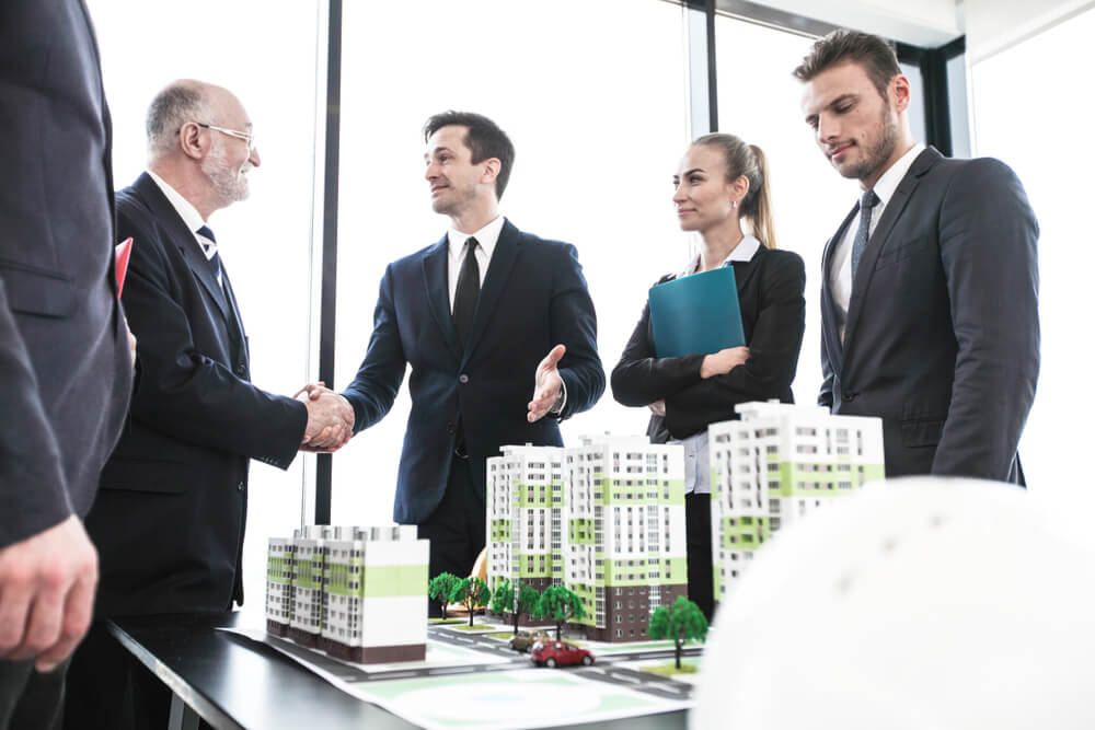 Business People Standing Near Residential Quarter Houses Models and Shaking Hands
